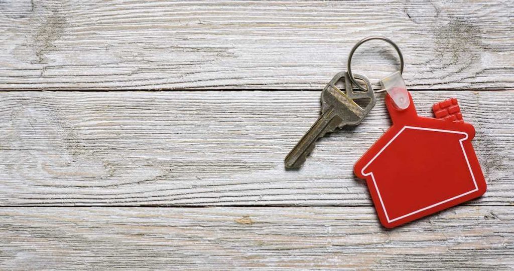 House key on a red-colored, house-shaped keychain resting on wooden floorboards